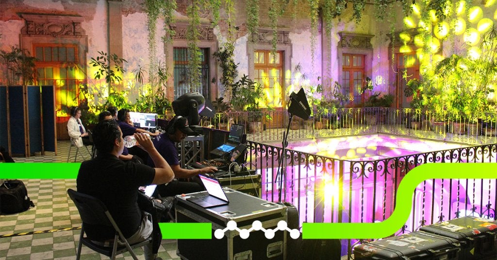 Técnicos operando iluminación y producción en un venue histórico, coordinando un evento en vivo con equipos audiovisuales y efectos de luz ambientales.