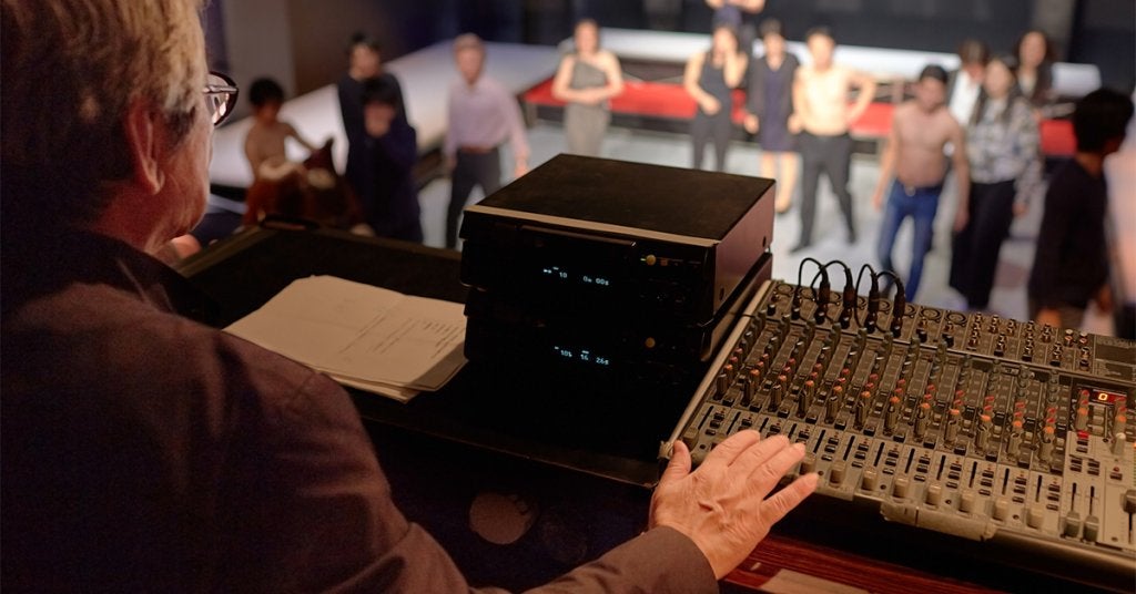 Profesional supervisa la operación técnica de un evento desde la cabina de control mientras el equipo trabaja en el escenario.