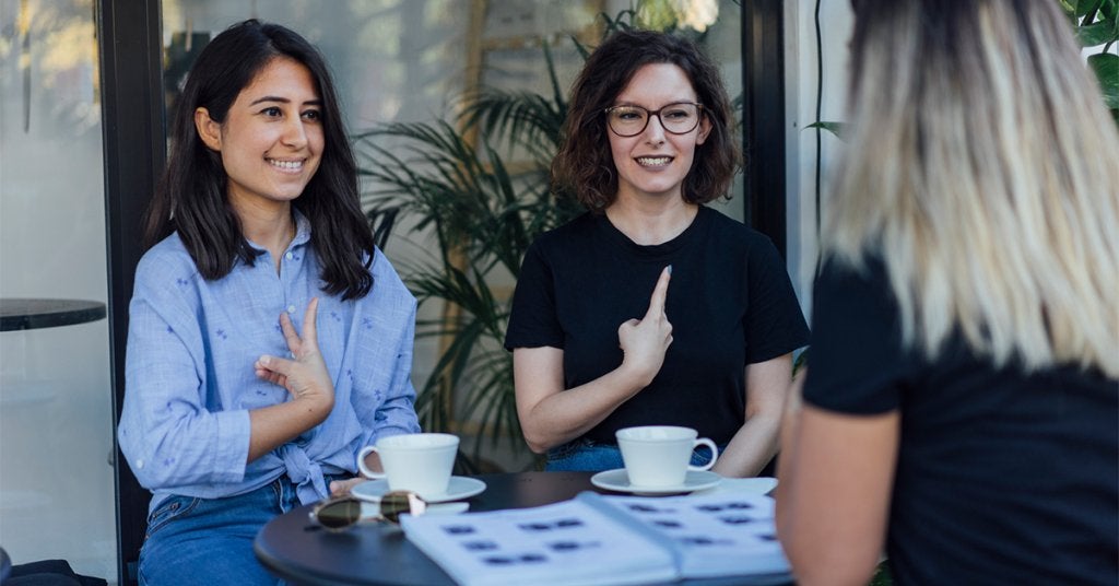 Tres personas participan en una conversación en un entorno relajado, reflejando distintas formas de comunicación e interacción dentro de una experiencia inclusiva.