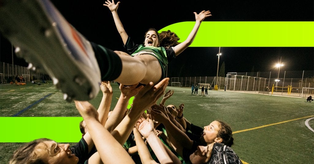 Equipo celebrando el éxito de un proyecto, levantando a una integrante como gesto de triunfo y camaradería tras lograr el objetivo en conjunto.