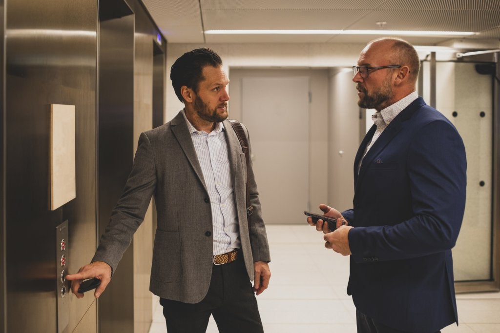 Dos ejecutivos conversan en un entorno corporativo mientras analizan una situación de negocio.