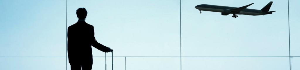 Man at airport with suitcase looking out at landing plane