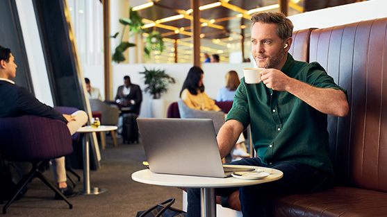 A male business traveller sits at a table in the Virgin Australia lounge with his laptop sipping a coffee