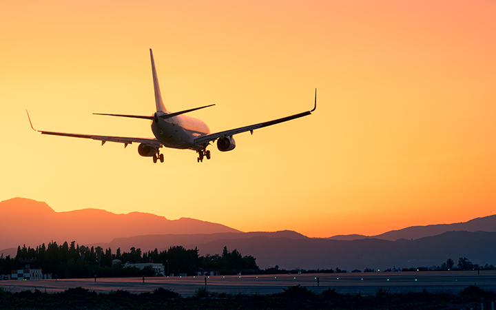 Jet plane silhouette approaching runway against orange sunset and mountain backdrop