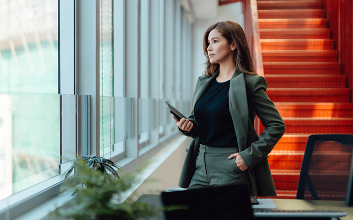 Businesswoman in green blazer holding phone by office window and red stairway