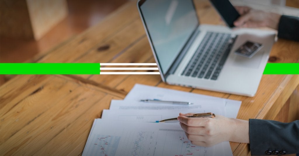 Mano señalando gráficos financieros junto a una laptop, representando el análisis del costo total del viaje y el crecimiento de los ingresos auxiliares.