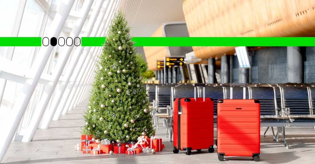 Árbol de Navidad junto a maletas rojas en una sala de aeropuerto, representando los retos de viajar en temporada alta con políticas poco flexibles.