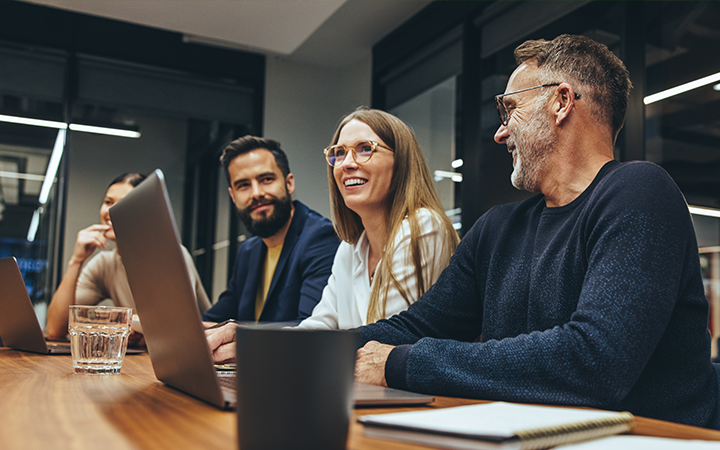Group of people at a board meeting, around a laptop