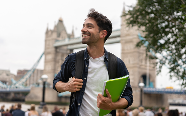 man smiling holding a green book with a bridge in the backgroun