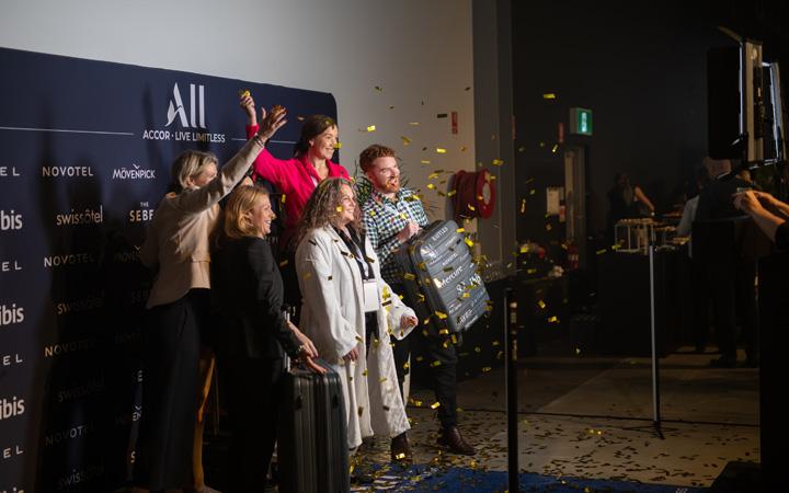 Side picture of a group of people standing for a photo against a backdrop cheering
