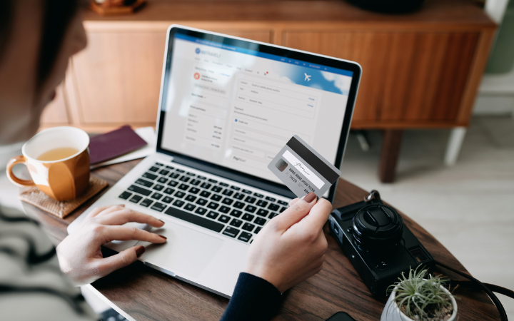 Person sitting in front of a laptop holding a credit card in their hand