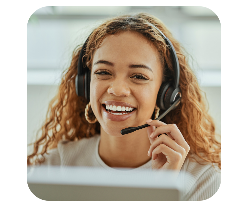 Photograph of a smiling young woman with curly hair wearing a headset at her desk