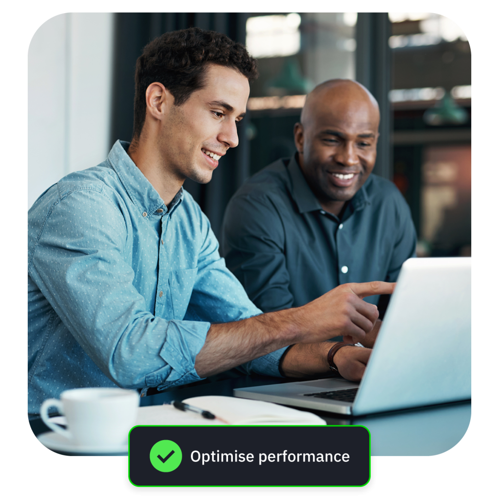 Photograph of two men at a cafe table smiling as they work on a laptop