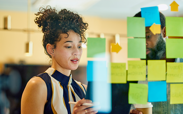 A woman and a man collaborating at a board covered with sticky notes planning and strategising smart business travel programs