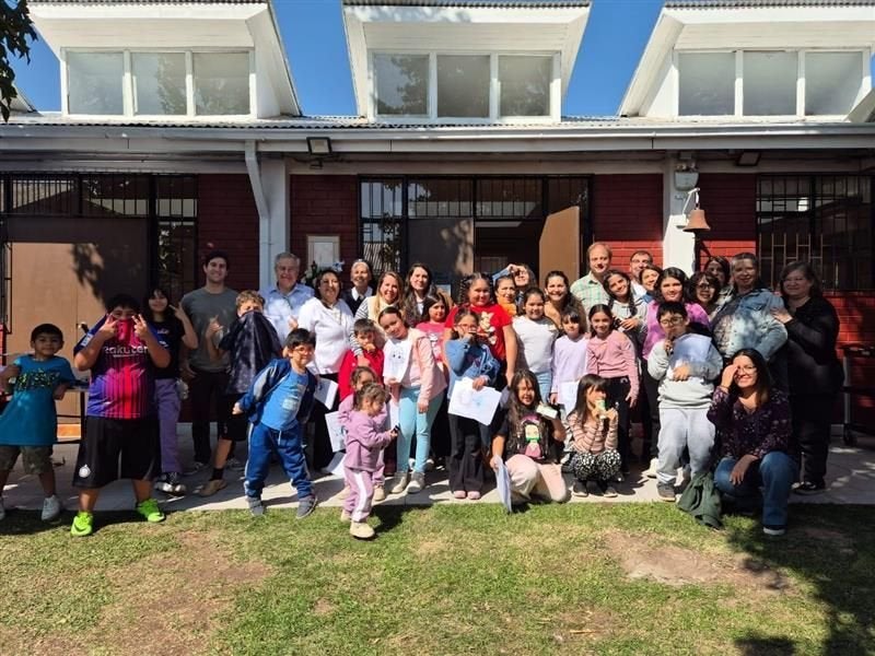 A large group of children and adults smiling together outside a building in sunny weather.