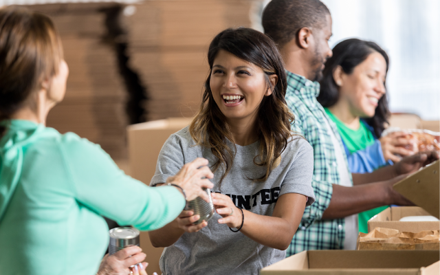 Smiling volunteers sort and pack canned food into cardboard boxes
