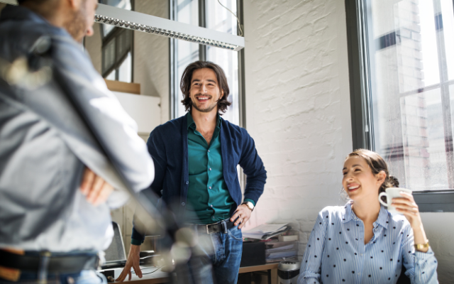 Three professionals engaged in conversation in a bright office setting.