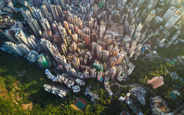 Aerial photograph of dense high-rise city skyline meeting lush green hillside