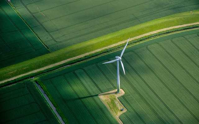 Aerial view of lone wind turbine casting shadow over green farmland grids
