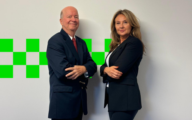 Two professionals smiling and posing confidently against a white wall with green checkered accents.