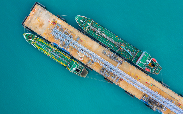 Two green cargo ships docked at a pier on turquoise water.