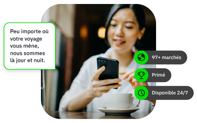 Femme souriante utilisant un smartphone dans un café, avec une tasse devant elle.