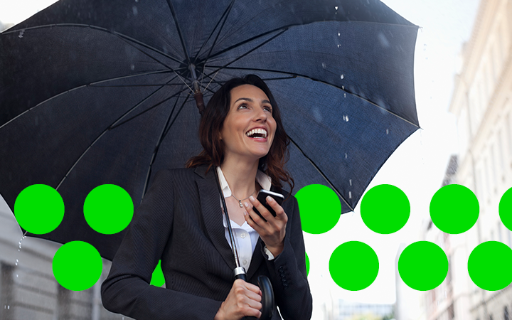 A woman walking in the rain, smiling, under an umbrella 