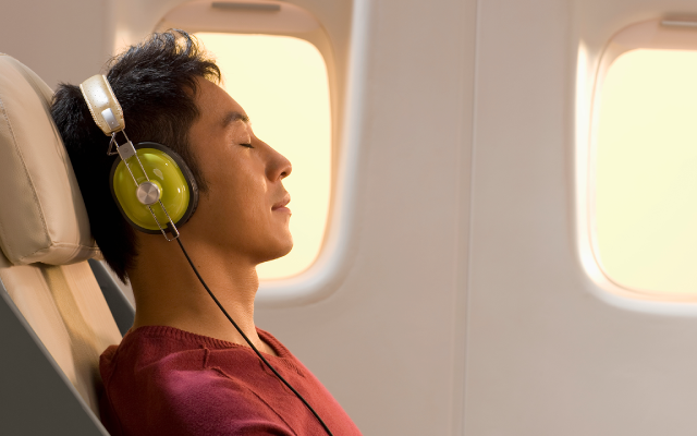 Passenger wearing green headphones reclines in airplane seat next to window