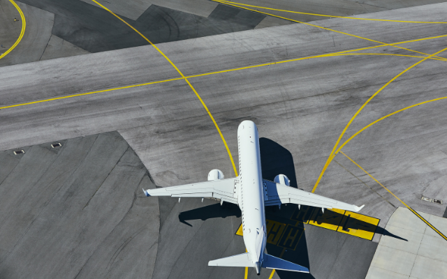 Aerial view of a white airplane on a taxiway with yellow marking lines.