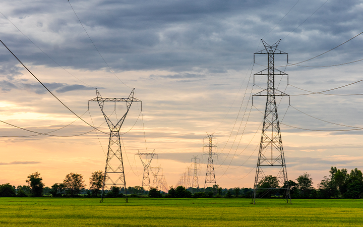 Power lines across green field at sunset