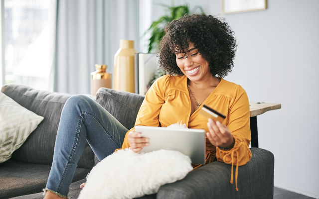 Smiling woman on couch reading a letter while holding a credit card