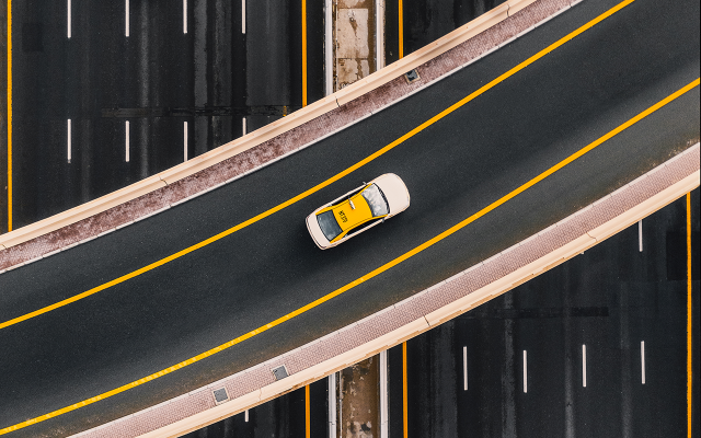 Aerial view of curved highway overpass with a yellow taxi in center lane