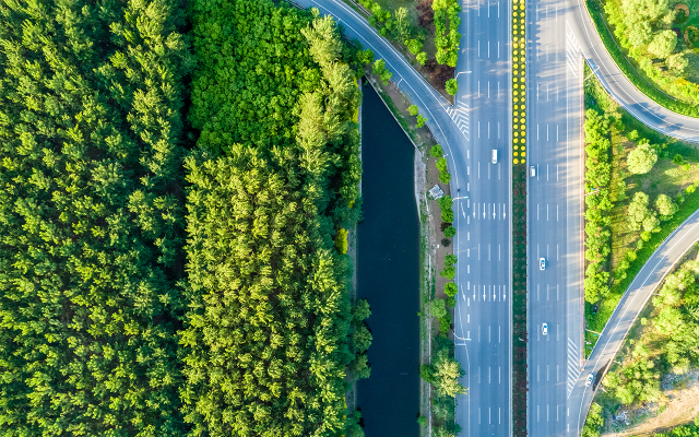 Aerial photograph of multilane highway over river slicing through green forest.