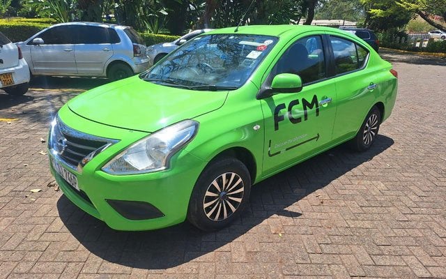Bright green FCM taxi sedan parked in a sunlit lot