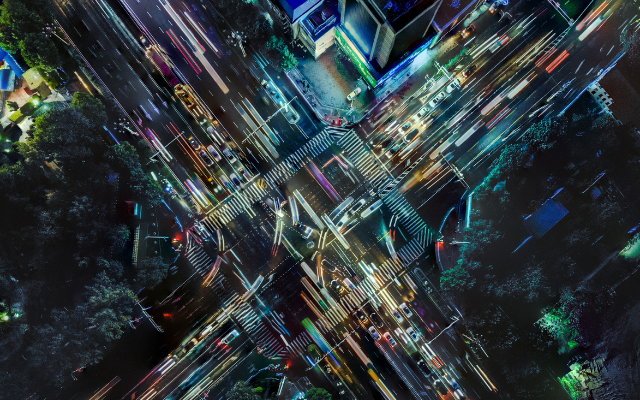 Aerial view of a busy intersection at night, with colorful light trails from moving vehicles.