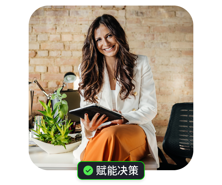 穿着白色外套的女性，微笑坐在办公桌前，手持平板，背景明亮。