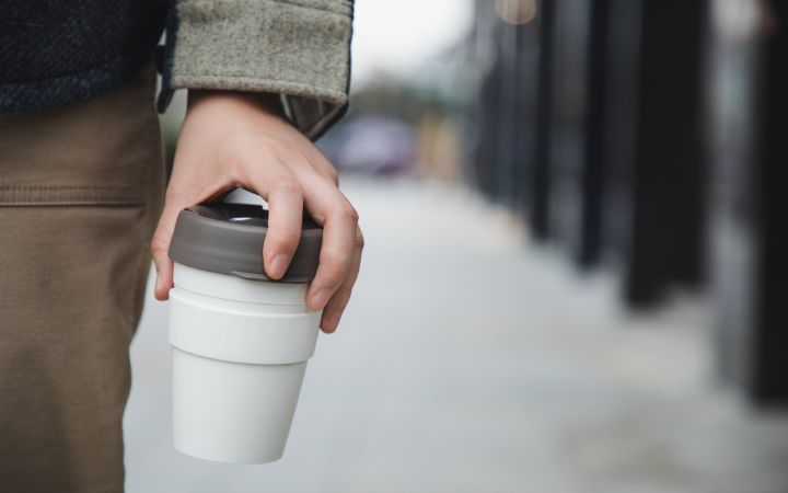 Hand holding reusable cup highlighting effective strategies for hosting responsible events that create a positive impact.