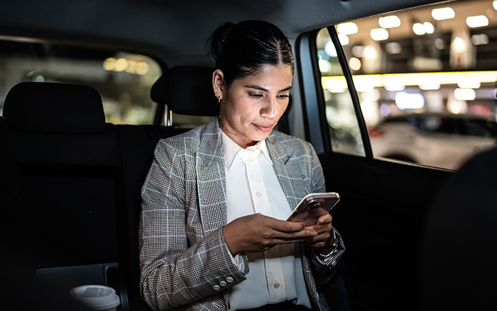 Person in backseat of car at night checking a paper map while holding a smartphone.