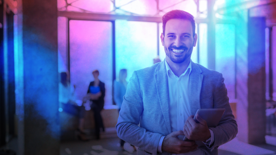 man smiling at camera with pink, purple and blue lighting 