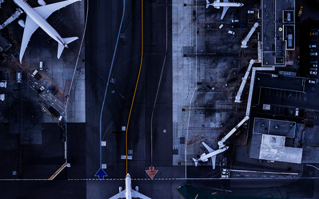 Aerial view of airport tarmac with airplanes at gates beside terminal.