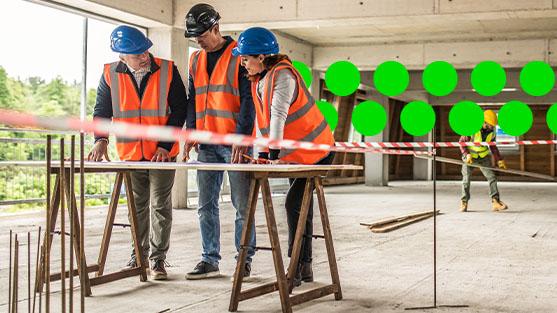 3 people standing on construction site looking at plans in highvis