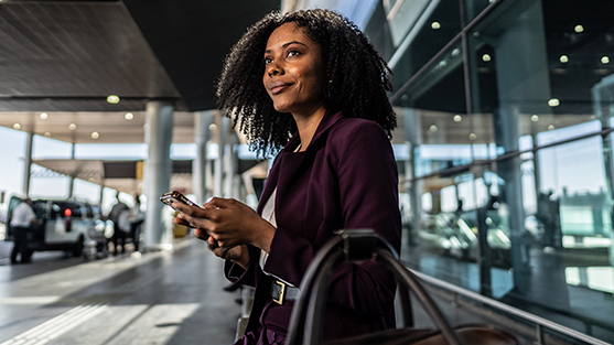 Woman in a purple outfit holding a phone, smiling at an airport terminal.