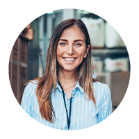 Smiling woman in striped shirt and lanyard standing before blurred warehouse shelves