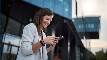 Woman in white blazer smiling at smartphone in modern urban setting