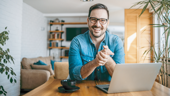 Man rubbing sore wrist while using smartphone and laptop at home desk.