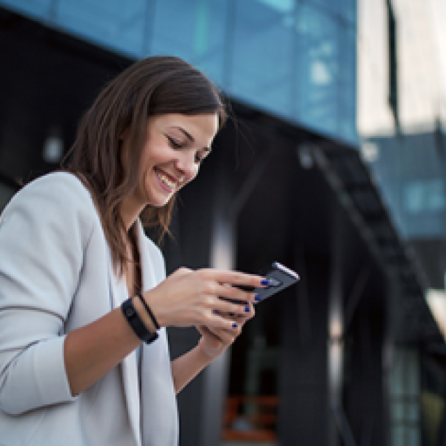 Woman in white blazer smiling at smartphone in modern urban setting